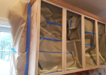 Kitchen cabinets masked with protective paper and blue painter’s tape ready for refinishing in Groton MA