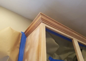 Close-up of upper wooden kitchen cabinet with crown molding and masking tape in Groton MA
