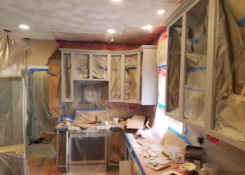 Kitchen cabinets masked with paper and plastic in a Groton kitchen during cabinet refinishing preparation
