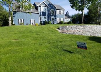 Large blue two-story house with manicured lawn and stone retaining wall in Groton Massachusetts