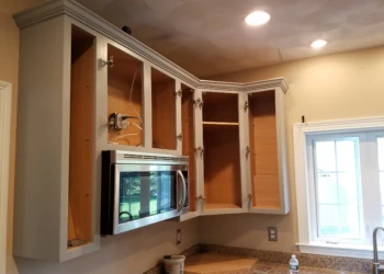 White upper kitchen cabinets without doors around a microwave above granite countertop in Groton kitchen