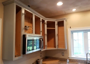 Partially refinished kitchen cabinets with open doors and installed microwave above granite countertop in Groton MA home