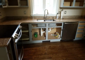 Opened kitchen base cabinets below granite countertop and stainless steel sink in home kitchen space