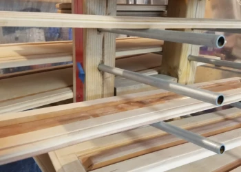 Wooden kitchen cabinet doors hung on rods in a workshop prior to refinishing in Groton MA
