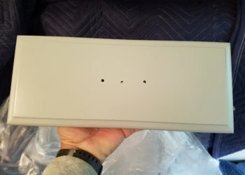 Close-up of a refinished light gray kitchen cabinet door with three pre-drilled holes, held by a hand