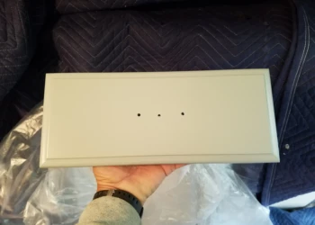 Hand holding a refinished light gray kitchen cabinet drawer front with three holes for knobs