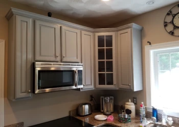 Light gray refinished kitchen cabinets above a corner countertop with microwave and kitchen appliances in Groton MA