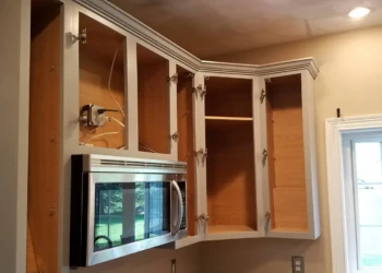Upper kitchen cabinets with open doors above a built-in microwave, showing unfinished wood interiors and white painted exteriors in Groton MA kitchen