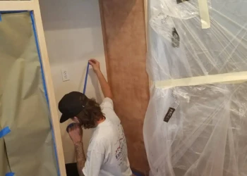 Worker applying blue painter's tape around kitchen cabinet edges during cabinet refinishing in Groton Massachusetts
