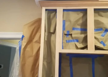 Kitchen cabinets masked with paper and blue painter's tape in preparation for refinishing in Groton MA