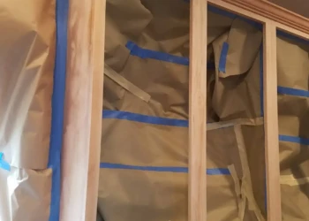 Wood kitchen cabinets with doors removed and interiors covered with paper and blue painter's tape for refinishing in Groton MA