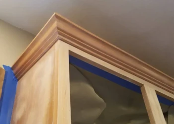 Close-up of wooden kitchen cabinet with protective blue tape and masking paper during cabinet refinishing in Groton MA