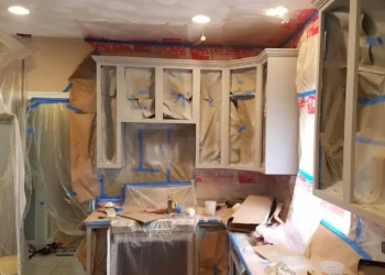 Kitchen cabinets in a Groton home prepped with protective paper and plastic covering surrounding areas for cabinet refinishing