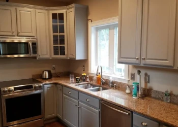Refinished kitchen cabinets under a window next to stainless steel sink and granite countertops in a Groton MA home
