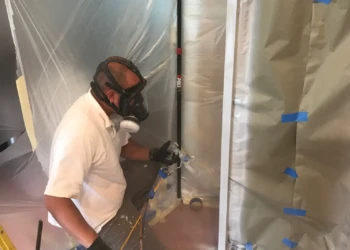 Finish Masters Builders worker using spray gun with protective mask preparing kitchen cabinets for refinishing in Groton MA