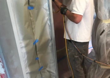 Worker using spray equipment to refinish kitchen cabinets with protective coverings in Groton MA home