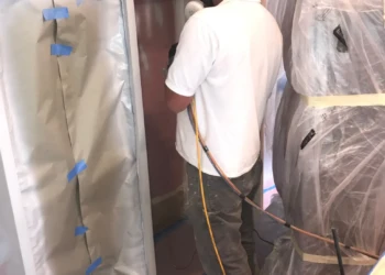 Worker wearing protective mask refinishing kitchen cabinets with spray equipment in Groton MA home