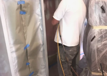 Worker wearing respirator spraying finish on kitchen cabinets during cabinet refinishing in Groton MA