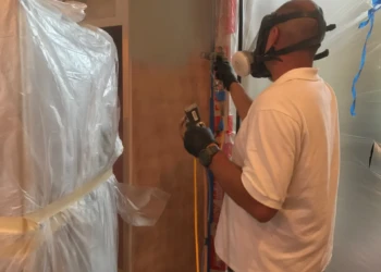 Worker wearing protective gear spraying finish onto kitchen cabinets in Groton MA