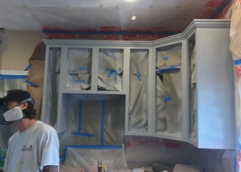 Kitchen wall cabinets covered and masked with paper and tape during cabinet refinishing in Groton MA