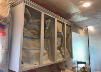 Upper kitchen cabinets masked with paper and tape for cabinet refinishing in a Groton MA home