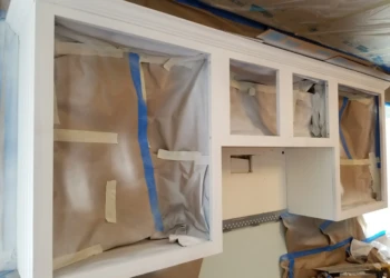 White kitchen wall cabinets with protective paper and painter's tape during cabinet refinishing in Merrimack, NH kitchen project