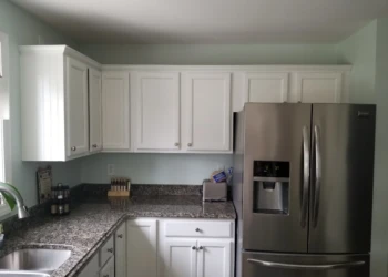 Freshly refinished white kitchen cabinets with silver handles above and below granite countertop in Merrimack kitchen