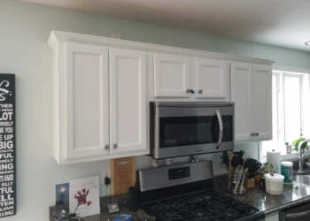 Freshly refinished white kitchen cabinets with crown molding above stainless steel microwave and stove in a Merrimack kitchen