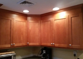 Unfinished natural wood kitchen cabinets corner set with metal knobs under recessed lighting