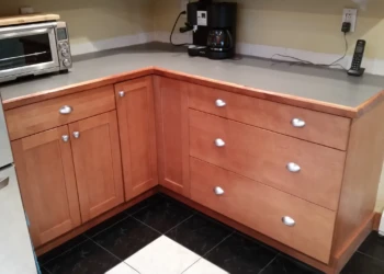 Cherry wood kitchen cabinets in an L-shape configuration with silver handles before refinishing in Nashua NH
