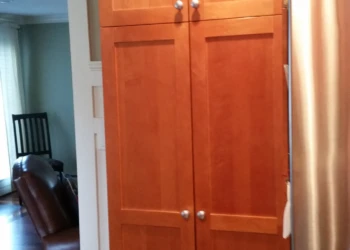Tall cherry wood pantry cabinets with four doors next to stainless steel refrigerator in a Nashua kitchen