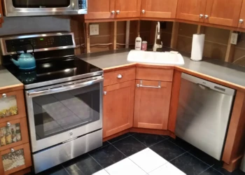 Cherry wood kitchen cabinets and stainless steel appliances in a kitchen before cabinet refinishing in Nashua NH