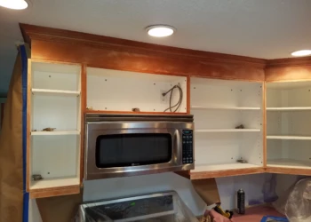 Kitchen cabinets with doors removed showing sanding preparation around a microwave in Nashua NH kitchen