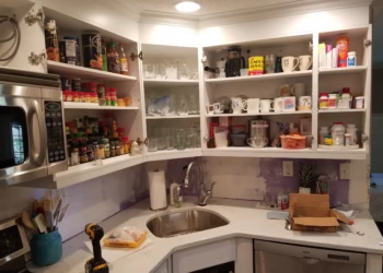 Open kitchen cabinets freshly refinished with white paint above countertop and stainless steel sink in Nashua NH kitchen