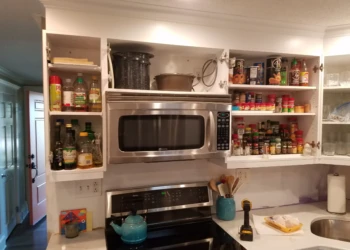 Open white kitchen cabinets around stainless steel microwave and stove showing organized spices and cooking oils in Nashua kitchen