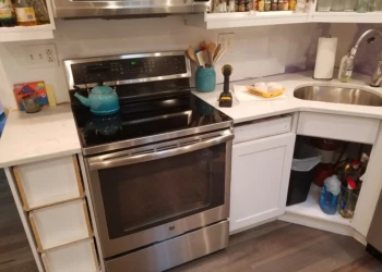 Partially refinished kitchen cabinets around stainless steel oven and sink with some cabinet doors removed in Nashua kitchen