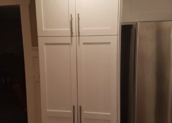 Tall kitchen pantry cabinets with smooth white refinishing and silver handles beside stainless steel refrigerator in Nashua
