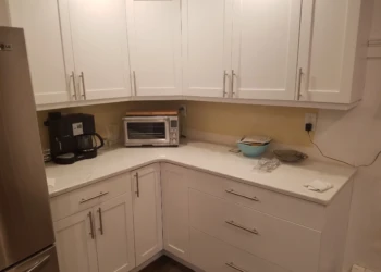 Corner kitchen view with white refinished cabinets, stainless steel refrigerator, coffee maker, toaster oven, and light counter