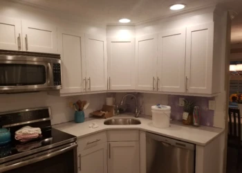 Newly refinished white kitchen cabinets with silver handles above and below a corner sink area in a Nashua kitchen