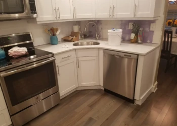 White refinished kitchen cabinets under countertop with stainless steel oven, microwave, and dishwasher in Nashua kitchen