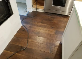 Dark wood flooring installed in a kitchen with white cabinets and stainless steel oven visible
