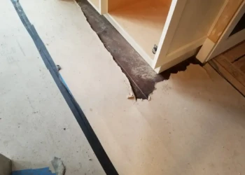 Damaged protective floor covering around kitchen base cabinets with drywall dust and paint drips in Newton MA.