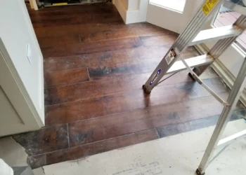 Close-up of dark stained custom cabinet doors and drawer fronts removed and laid flat with exposed hardware and a step ladder nearby