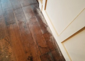 Close-up of kitchen cabinet base and dark wood floor with visible dust and finishing residue in Newton home remodel