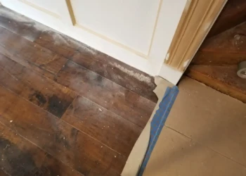 Close-up of the base of a custom kitchen cabinet with refinishing work showing minor wear and dust on the hardwood floor nearby