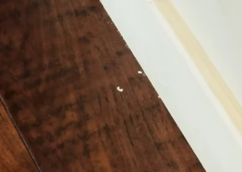 Close-up of a dark stained wooden cabinet surface with minor imperfections near a white baseboard