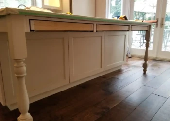 Close-up of newly refinished kitchen island cabinets with freshly painted cream doors and unfinished drawer fronts in Newton MA