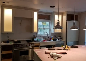 Kitchen cabinets in mid-refinishing stage with some cabinet doors removed and tools on the countertop