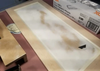 A disassembled wooden cabinet door laid flat on a workbench, showing its bare wood surface prepared for refinishing in Newton MA.