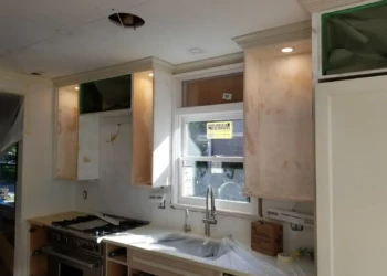 Unfinished custom kitchen cabinets with some areas sanded and prepped around a window and stove in Newton MA kitchen remodeling